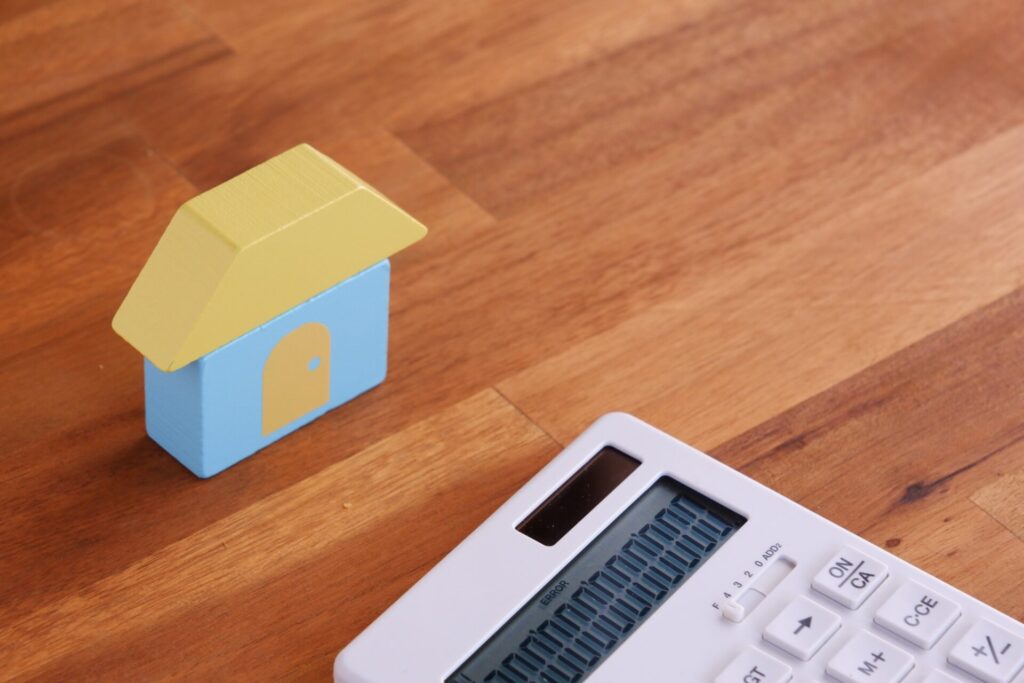 家と電卓で、あこがれのマイホームを購入するために資金計画を立てているイメージ